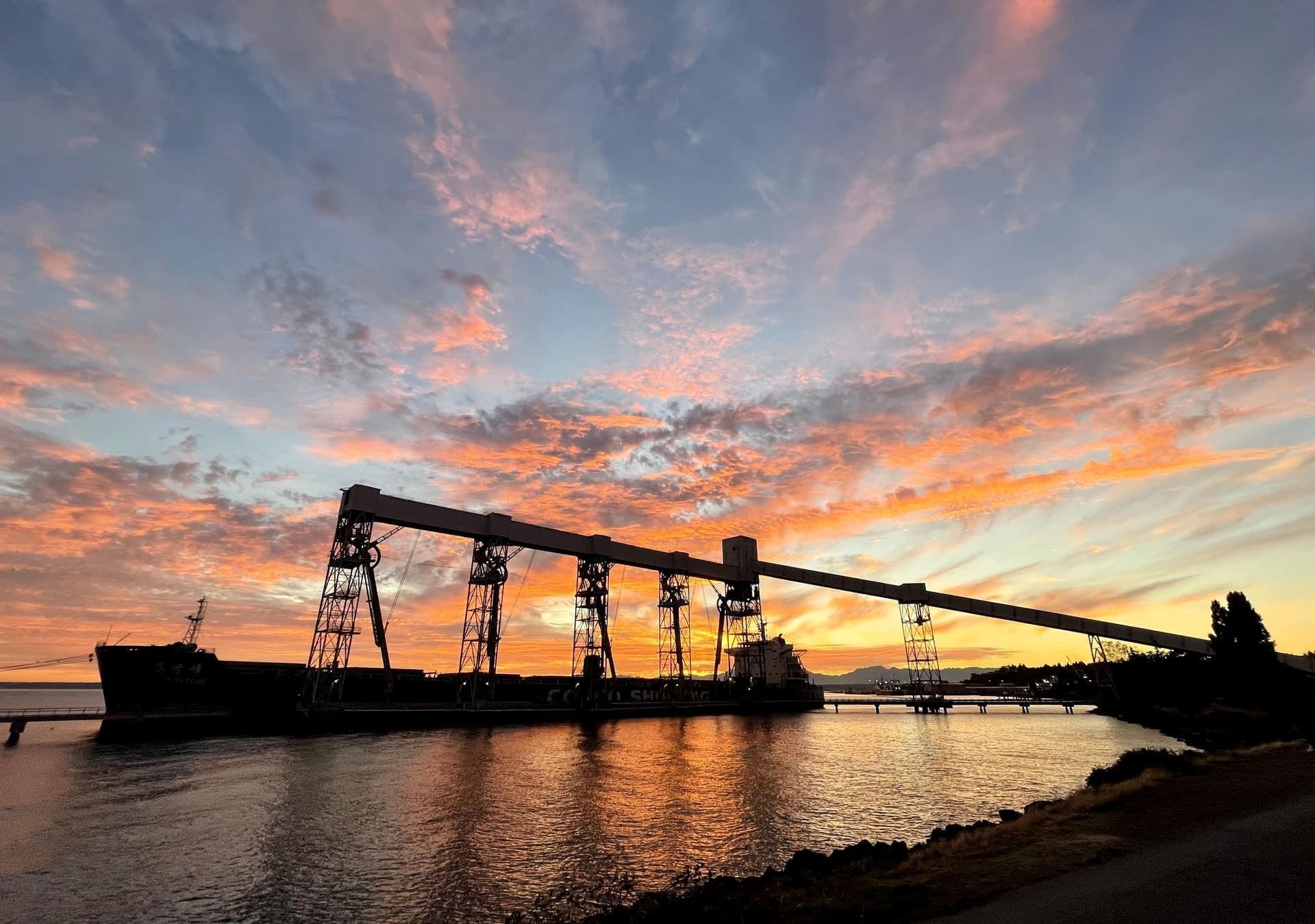A modern dry bulk carrier silhouetted against the sunset at a grain terminal